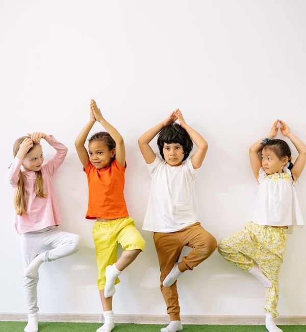 Child smiling while doing a stretching yoga pose indoors.